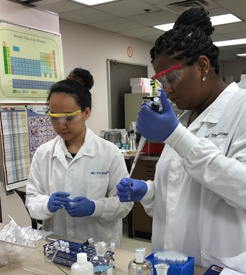 Two students in lab coats and goggles in a lab