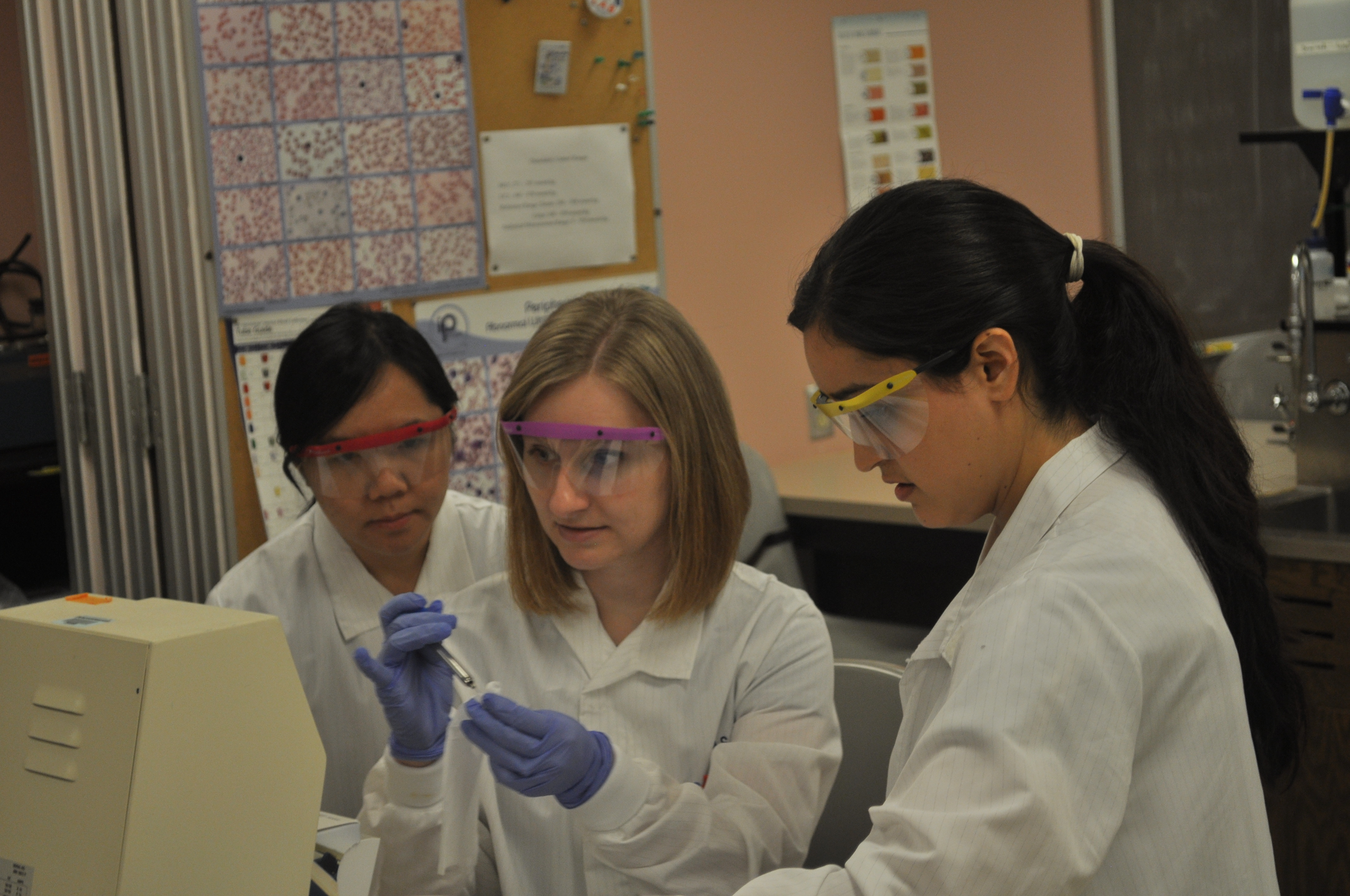 Three students in lab coats and protective glasses